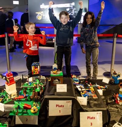 3 Kinder hinter ihren ausgezeichneten Lego Bauwerken. Sie sind die Gewinner des Lego Wettbewerbs.